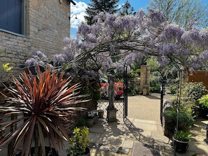 Un jardín con muro de piedra, un arco de metal y diversas plantas en macetas.