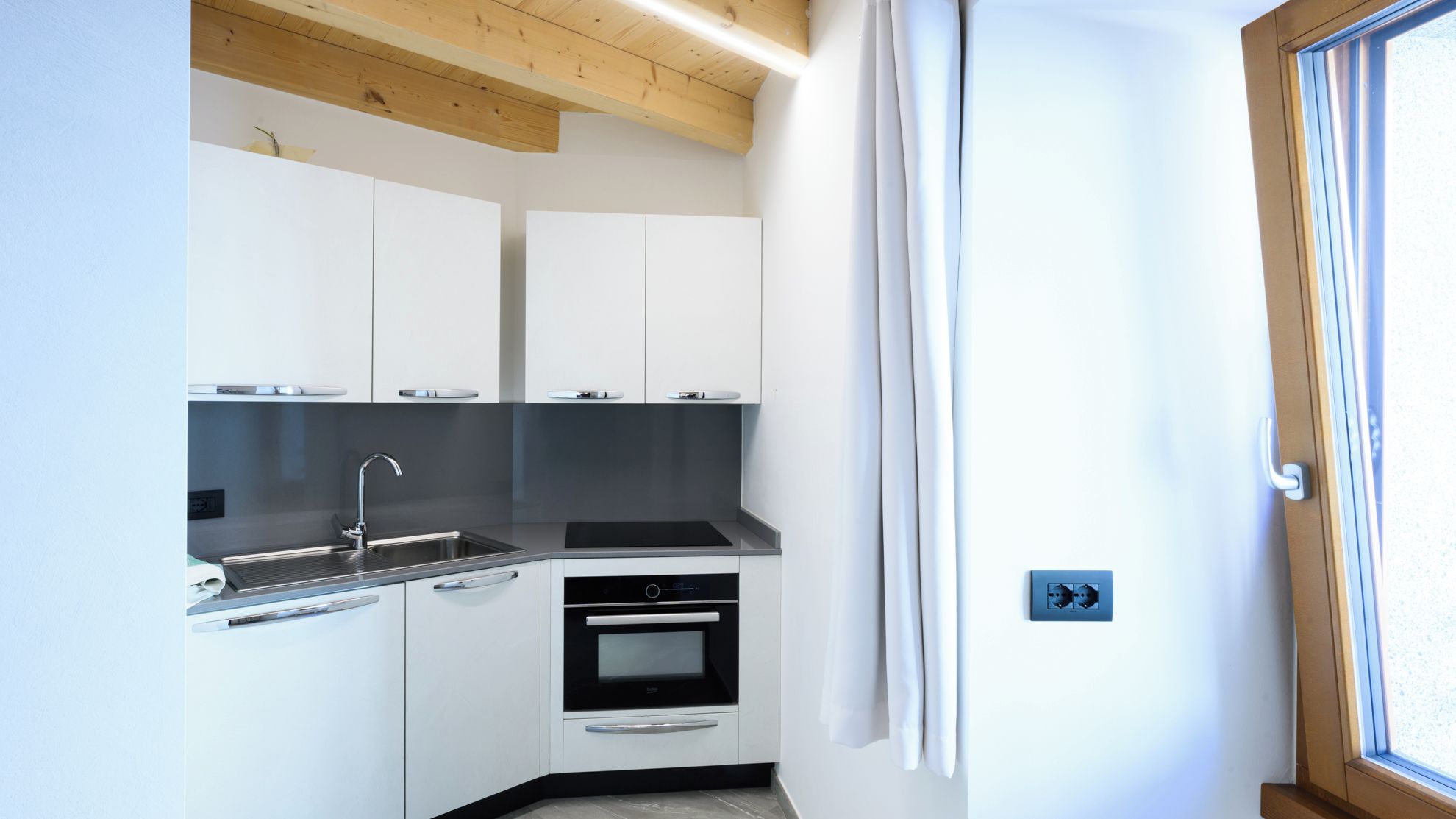 A compact kitchen with white cabinets, a black countertop, a sink, and an oven.