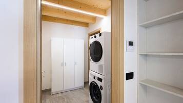 A laundry room with a stacked washer and dryer, a white door, and a wooden ceiling.