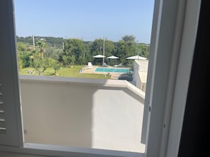 A balcony with a view of a swimming pool, trees, and a clear sky. - Detached Villa for Exclusive Use with an Infinity Pool (Puglia)