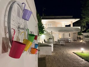 A bicycle with colorful buckets attached to its frame, a stone building with a white facade, and outdoor seating area. - Detached Villa for Exclusive Use with an Infinity Pool (Puglia)