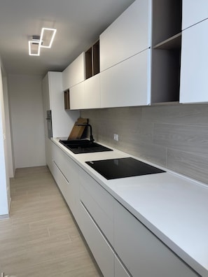 A modern kitchen with white cabinetry, a black induction cooktop, and a wooden countertop. - Detached Villa for Exclusive Use with an Infinity Pool (Puglia)