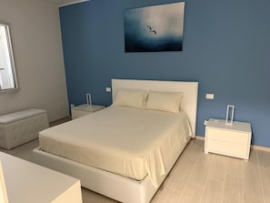 A bedroom with a large bed, two bedside tables, a nightstand, a bench, and a painting on the wall. - Detached Villa for Exclusive Use with an Infinity Pool (Puglia)