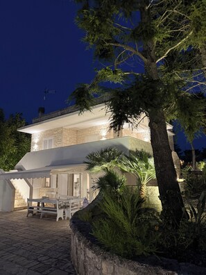 A two-story building with a stone facade, a covered outdoor seating area, and a large tree in the foreground. - Detached Villa for Exclusive Use with an Infinity Pool (Puglia)