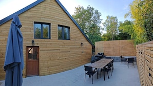 Eine Holzhütte mit einer Terrassenfläche, einem Grill und Sitzgelegenheiten im Freien.