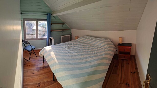Ein Schlafzimmer mit einem Bett, einem Sessel, einem Nachttisch und einem Fenster.