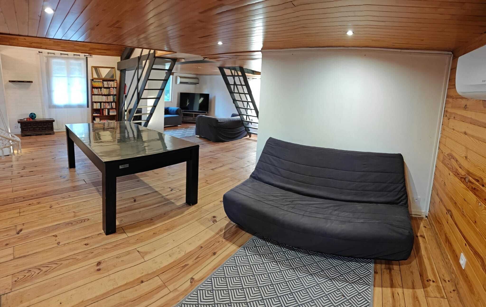 Un espacio habitable moderno con una mesa de vidrio, un sofá negro, un tapete estampado y suelo de madera.