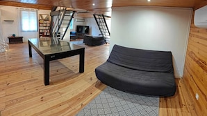Ein moderner Wohnraum mit Glastisch, schwarzem Sofa, gemustertem Teppich und Holzboden.