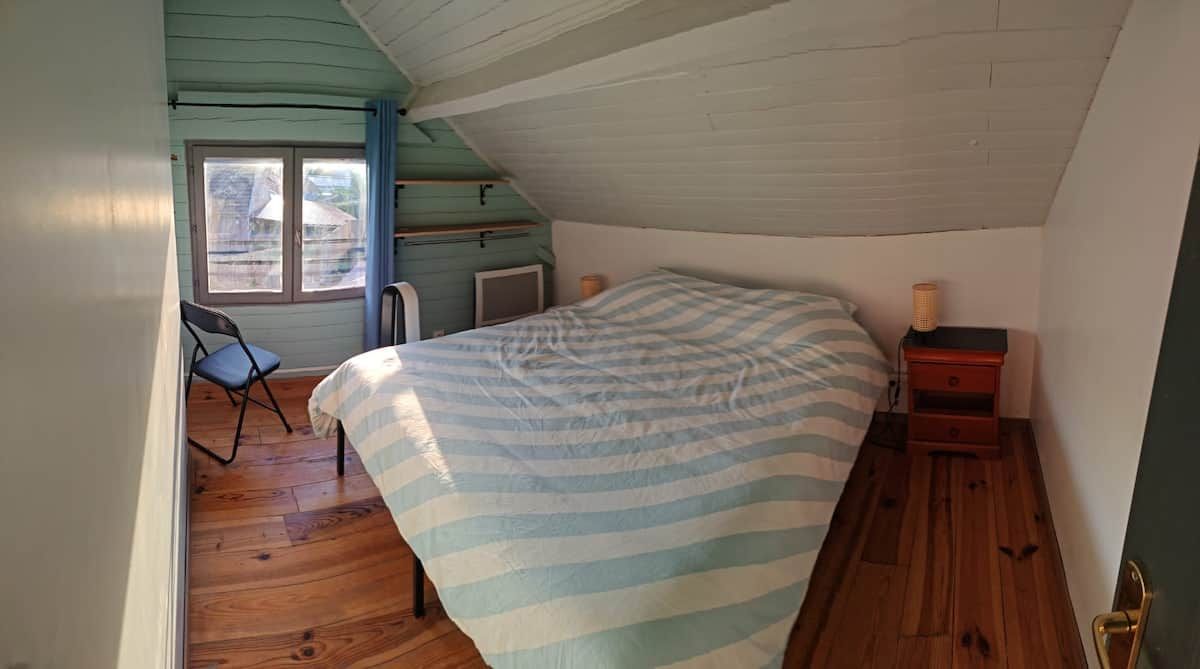 A bedroom with a bed, a chair, a nightstand, and a window.