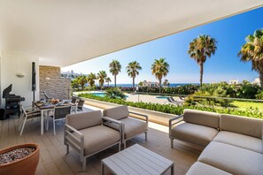 Ein Balkon mit Gartenmöbeln, einem Grill und Blick auf einen Pool und Palmen.