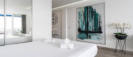 Une chambre d’hôtel moderne avec un grand lit, un tableau, une orchidée en pot et une horloge au mur.