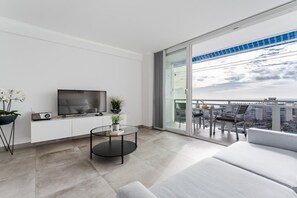 Ett modernt vardagsrum med en platt-TV, ett runt soffbord i glas och en soffa.