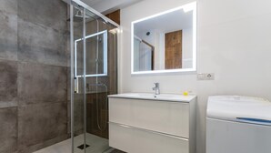 A modern bathroom with a glass shower enclosure, a white sink with a mirror above, and a white washing machine. - Studio in Costa del Sol, Torremolinos (Torremolinos)