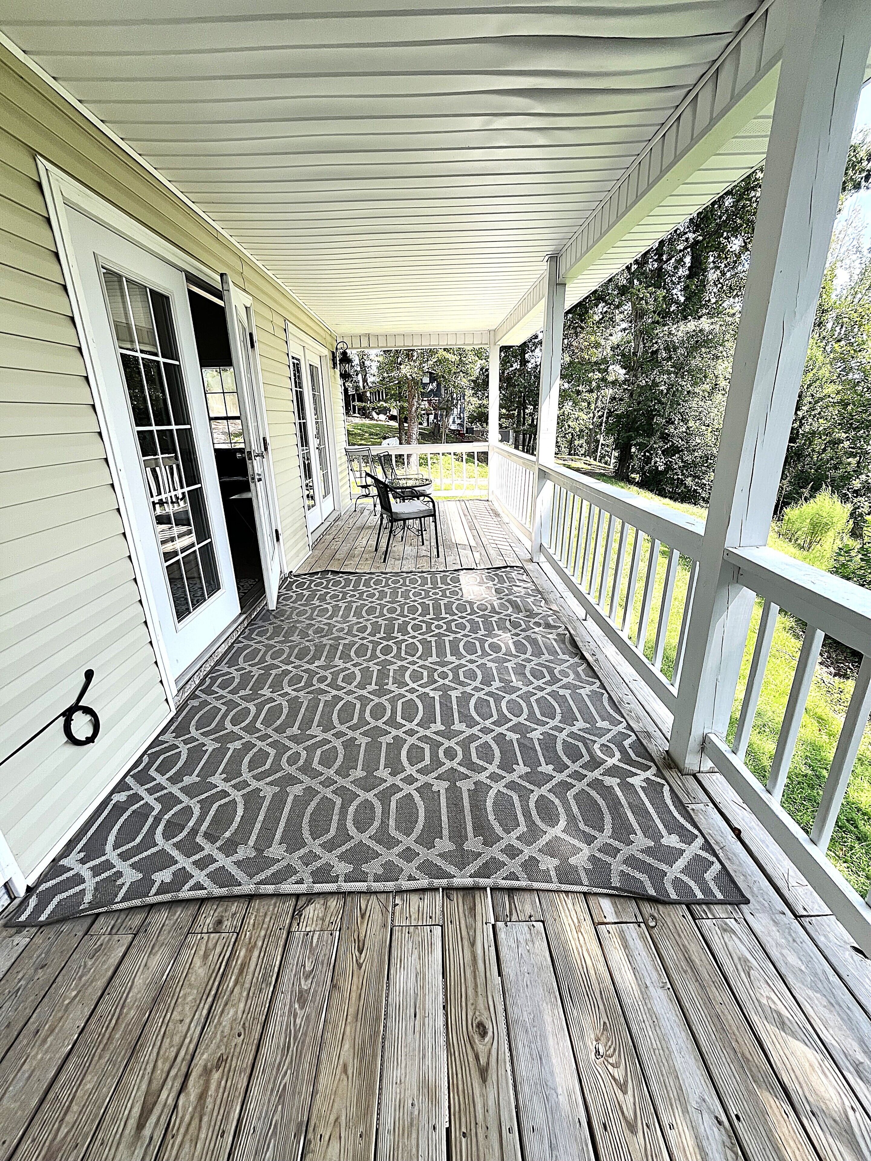 A covered porch with a patterned rug, a table with chairs, and a view of the neighborhood.