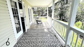 A covered porch with a patterned rug, a table with chairs, and a view of the neighborhood.