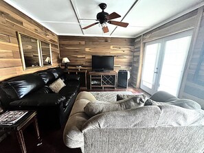 A living room with a black leather sofa, a beige sofa, a television, and a ceiling fan. - Rustic 4 bedroom Cabin Near Safe Harbor Aqua (Iuka)