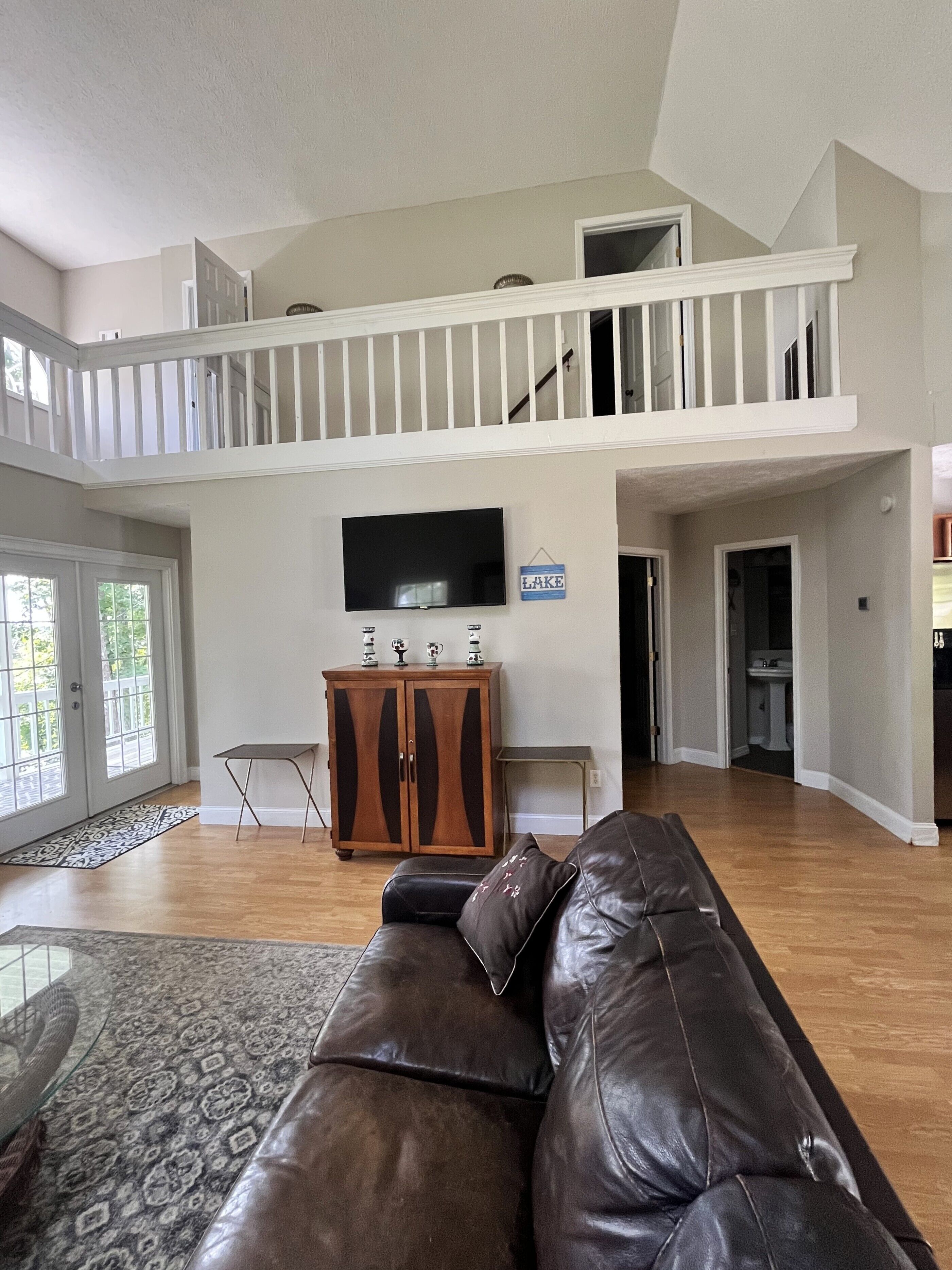 A spacious living room with a leather couch, a flat-screen TV, and a wooden cabinet.