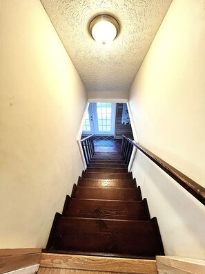 A wooden staircase with a handrail, leading to a landing with windows. - Rustic 4 bedroom Cabin Near Safe Harbor Aqua (Iuka)
