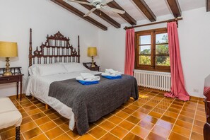 A bedroom with a wooden bed, two bedside tables with lamps, a window with curtains, and a radiator. - Charming Chalet for 8 in Pollensa (Pollença)