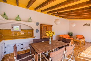 A dining area with a wooden table and chairs, a kitchen with a tiled backsplash, and a ceiling with exposed beams. - Charming Chalet for 8 in Pollensa (Pollença)
