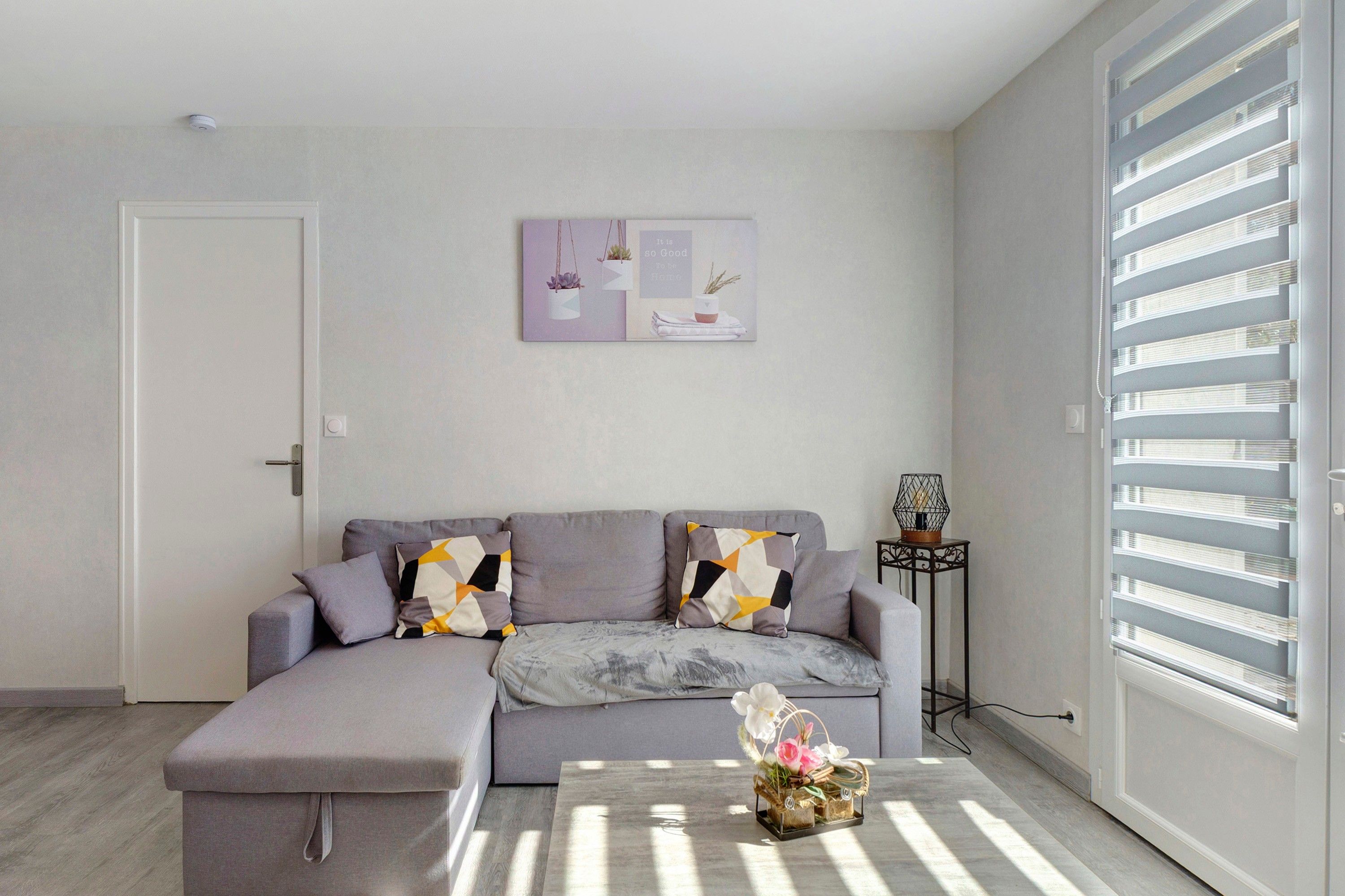 A modern living room with a grey sectional sofa, a small table with a basket of flowers, and a wall-mounted picture.
