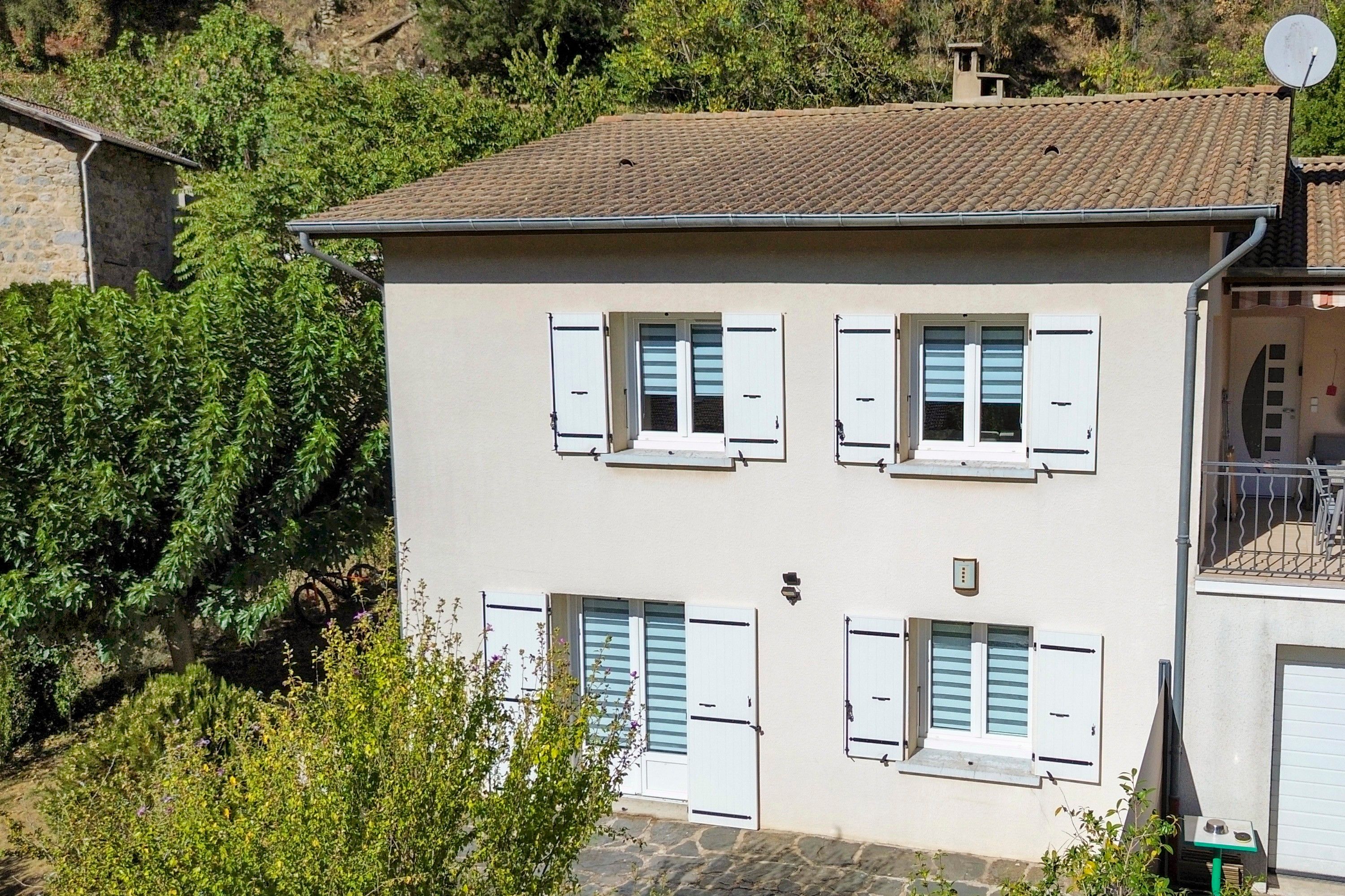 Un bâtiment à deux étages aux murs et volets blancs, entouré de verdure.