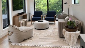 A modern living room with a large window, two armchairs, a sofa, a coffee table, and a television. - Modern house: Hot Tub Near Skiing & Harbor Springs (Harbor Springs)
