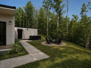 A modern outdoor area with a concrete pathway leading to a seating area with chairs and a fire pit. - Modern house: Hot Tub Near Skiing & Harbor Springs (Harbor Springs)