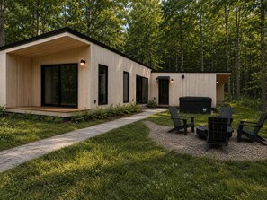 Una cabaña moderna con un porche cubierto, un jacuzzi y mobiliario de exterior.
