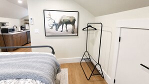 A bedroom with a bed, a bedside table, a wall-mounted artwork of a deer, a coat rack, and a door. - Riverbend Studio | Near Old Town & Poudre Trail (Fort Collins)