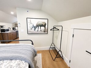 Quarto com cama, mesa de cabeceira, obra de arte na parede retratando um veado, porta-roupas e uma porta.