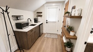 A modern kitchen with a microwave, coffee maker, and sink. There are wooden cabinets and a black floor lamp. - Riverbend Studio | Near Old Town & Poudre Trail (Fort Collins)