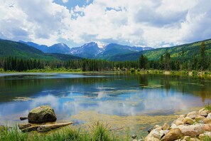 Un paisaje montañoso con un lago, cielos despejados y una gran roca en primer plano.