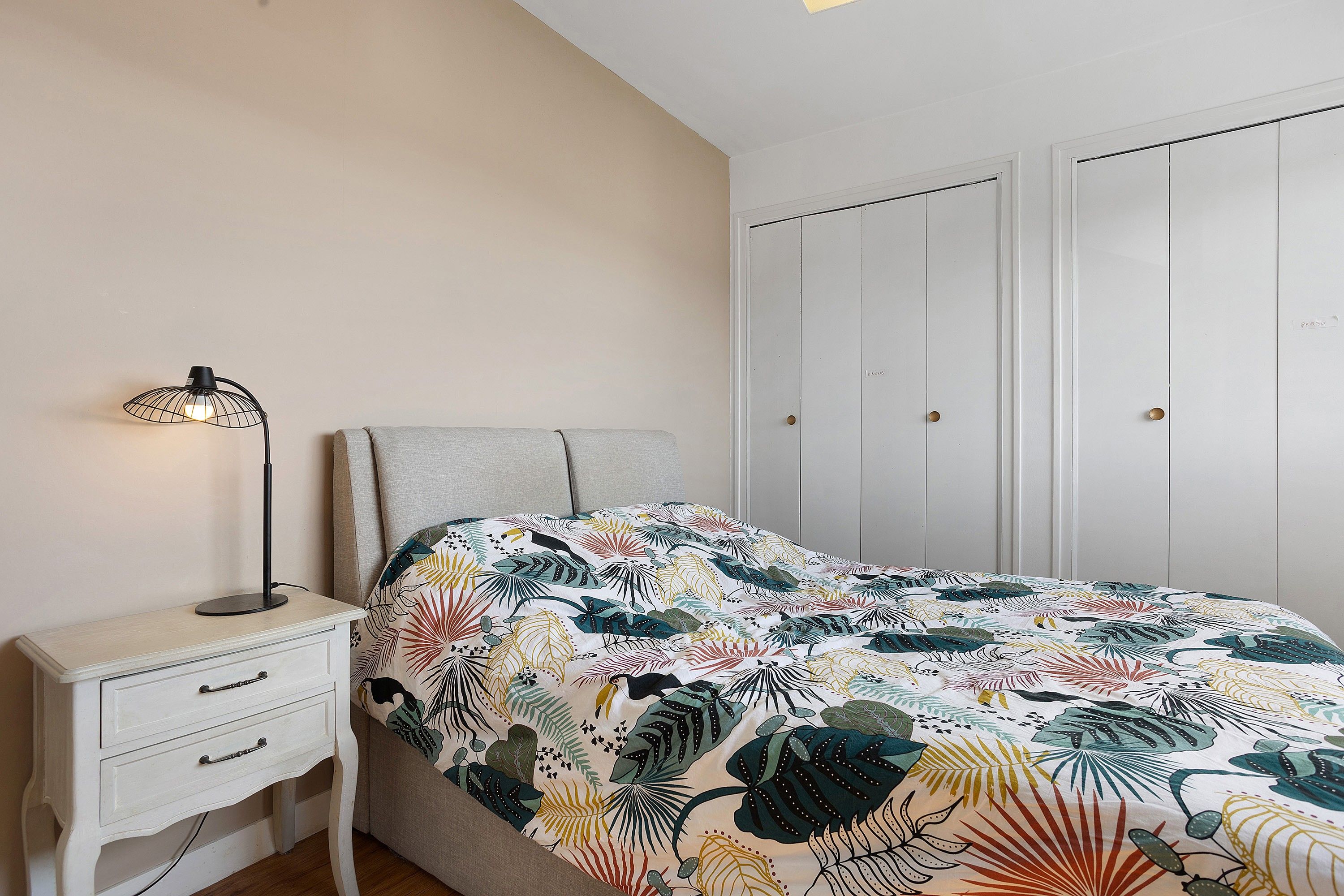 Une chambre à coucher comprenant un lit, une table de chevet avec des tiroirs, une lampe et une armoire.