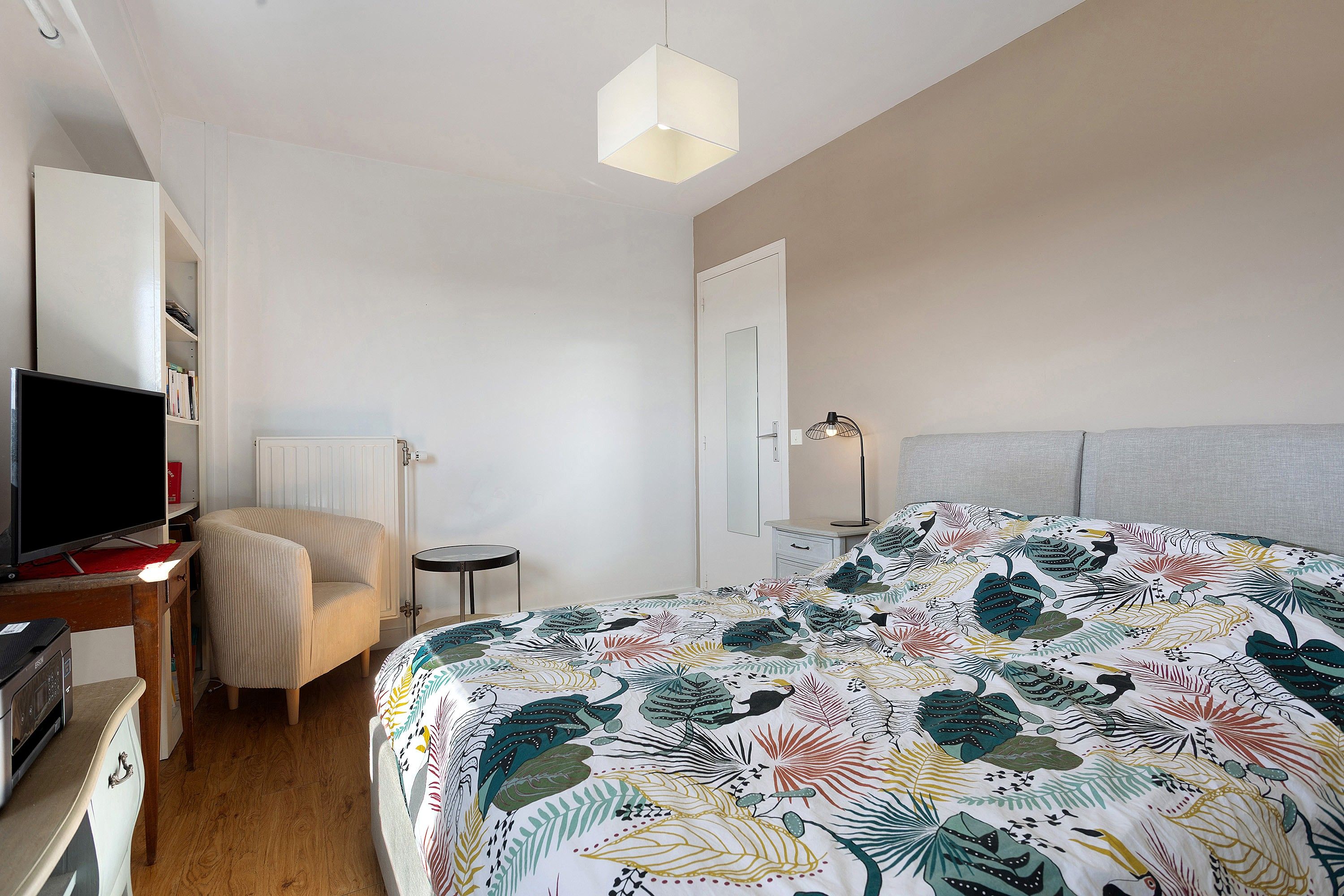 Een slaapkamer met een bed, een stoel, een bureau met een computer, een televisie en een bedlamp.