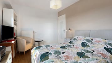 Een slaapkamer met een bed, een stoel, een bureau met een computer, een televisie en een bedlamp.