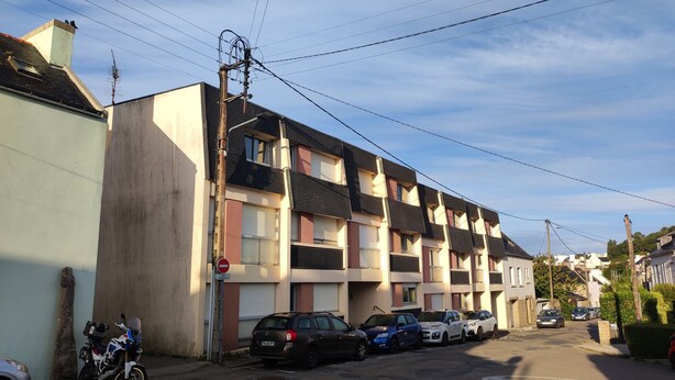 A residential street with a row of townhouses, parked cars, and a motorcycle. - “Croas Men” Apartment with Sea View and Wi-Fi (Douarnenez)