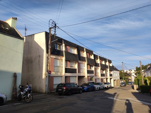 Une rue résidentielle bordée de maisons de ville, avec des voitures garées et une moto.