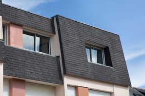 A multi-story building with a dark shingle roof and two visible windows.