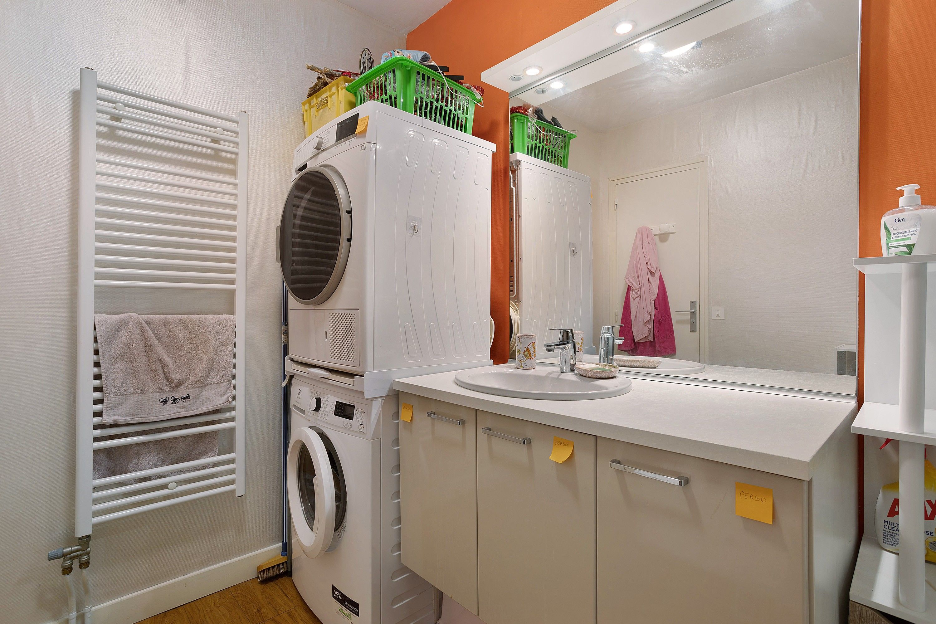 Une petite salle de bain équipée d’un lave-linge, d’un lavabo et d’un miroir.