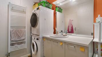 Une petite salle de bain équipée d’un lave-linge, d’un lavabo et d’un miroir.
