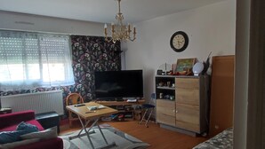 A living room with a television, a wooden cabinet, a red sofa, and a patterned sofa. - “Croas Men” Apartment with Sea View and Wi-Fi (Douarnenez)