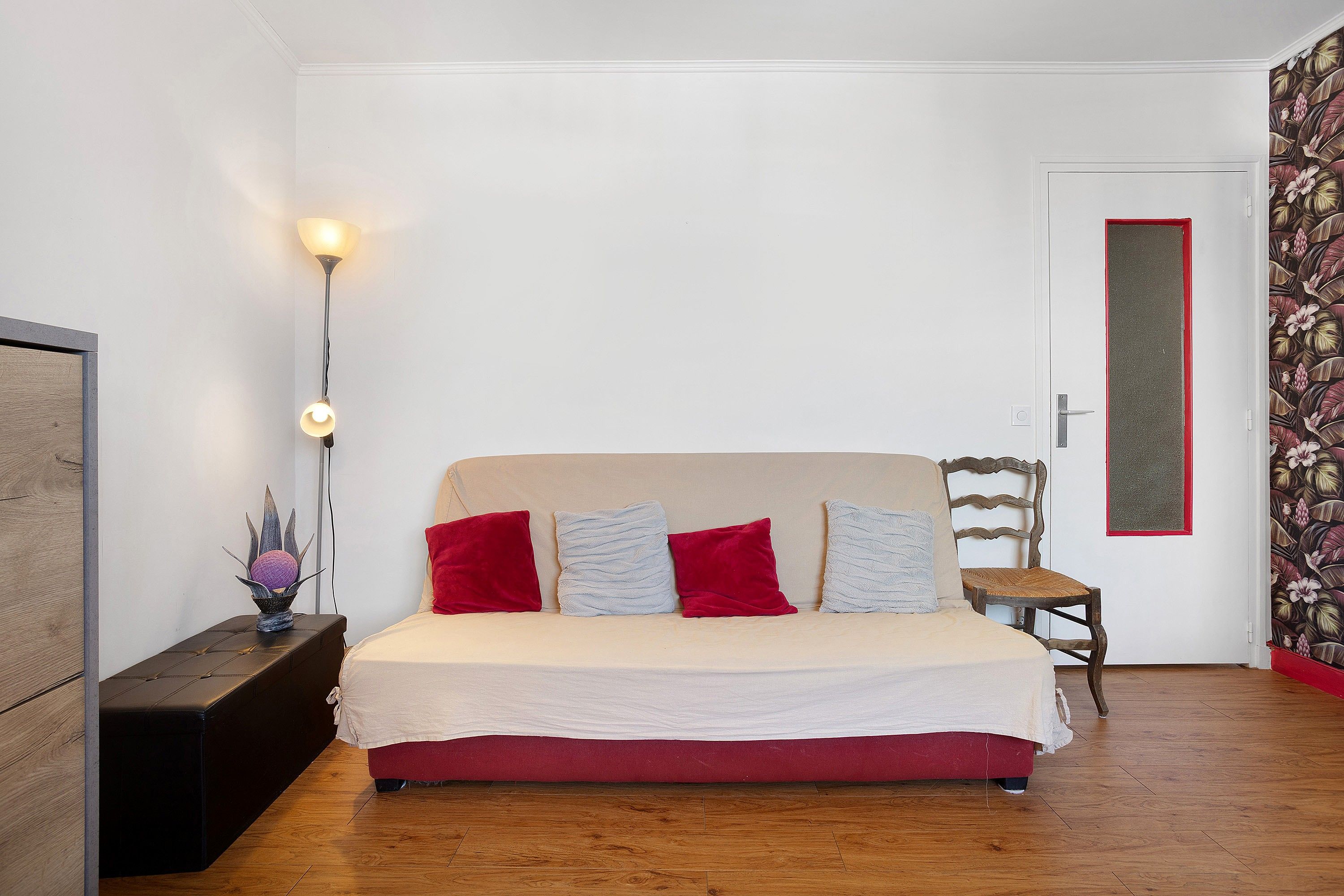 Una camera da letto con un letto, una sedia, un comodino, una lampada e una porta.