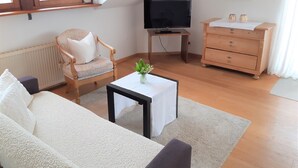 Ett mysigt vardagsrum med en soffa, en fåtölj, ett litet bord med en vas, en tv och en byrå.