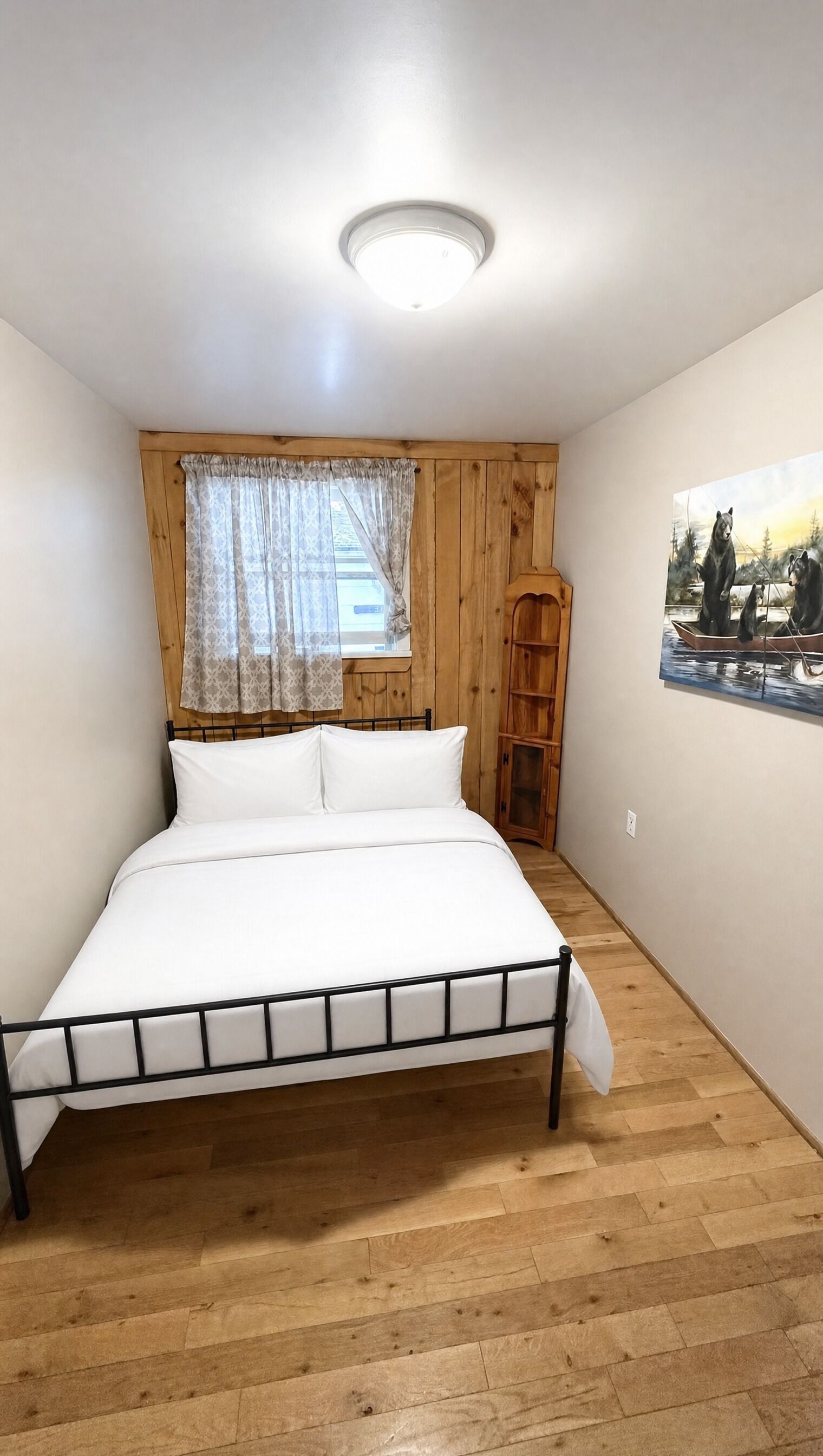 Une chambre à coucher avec un lit, des murs en bois, une fenêtre avec des rideaux, un luminaire au plafond et un tableau accroché au mur.