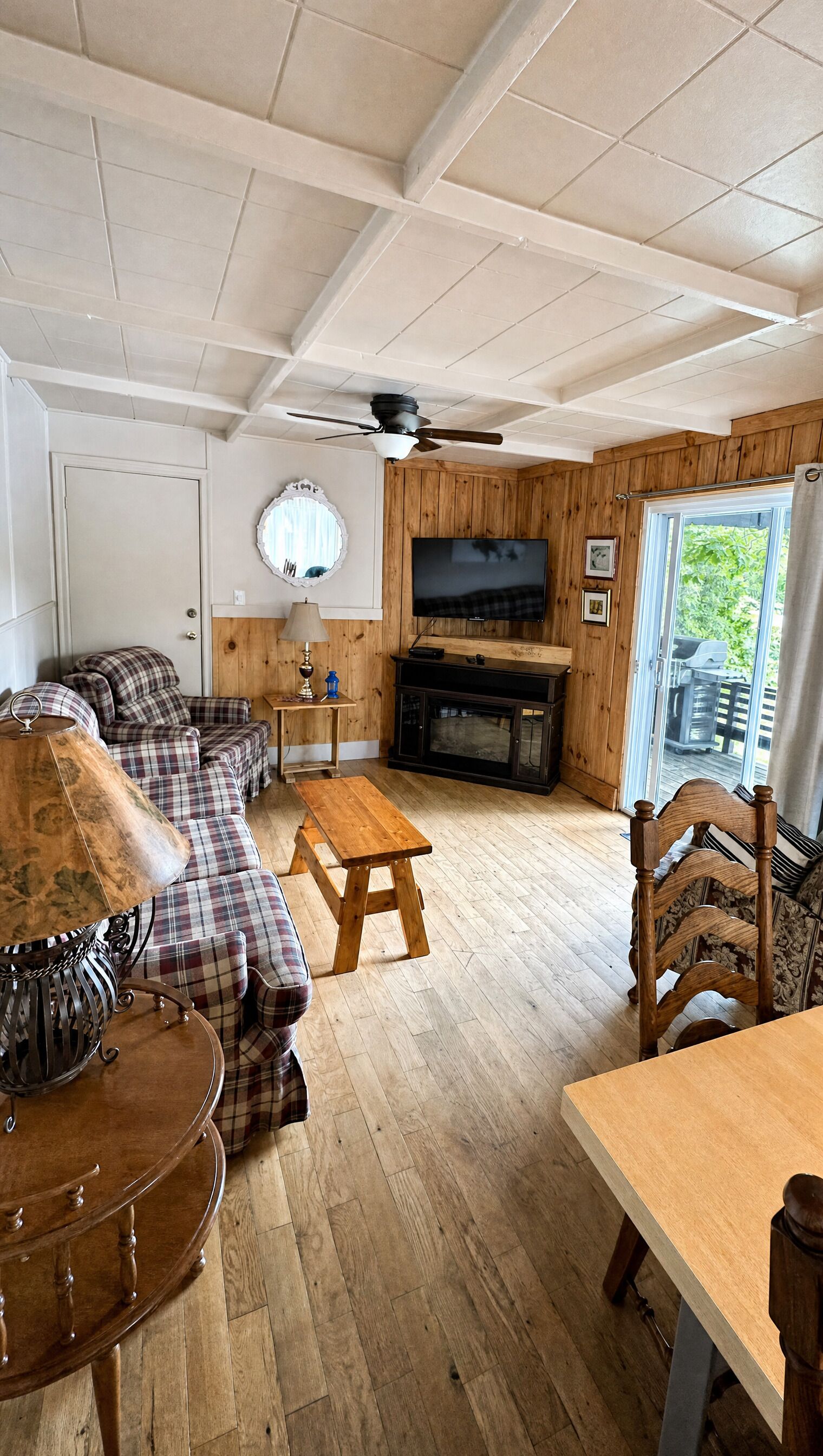A cozy living room with a sofa set, a wooden coffee table, a TV mounted on the wall, and a ceiling fan.