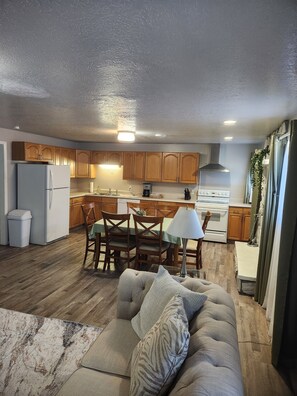 A modern kitchen with wooden cabinets, a dining area with a table and chairs, and a living room with a sofa and a rug.