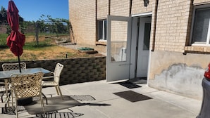 Una zona patio con tavolo e sedie, un ombrellone rosso e un'auto parcheggiata nelle vicinanze.