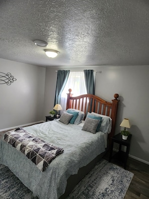 A bedroom with a bed, nightstands, a window with curtains, a ceiling light, and a wall decoration.
