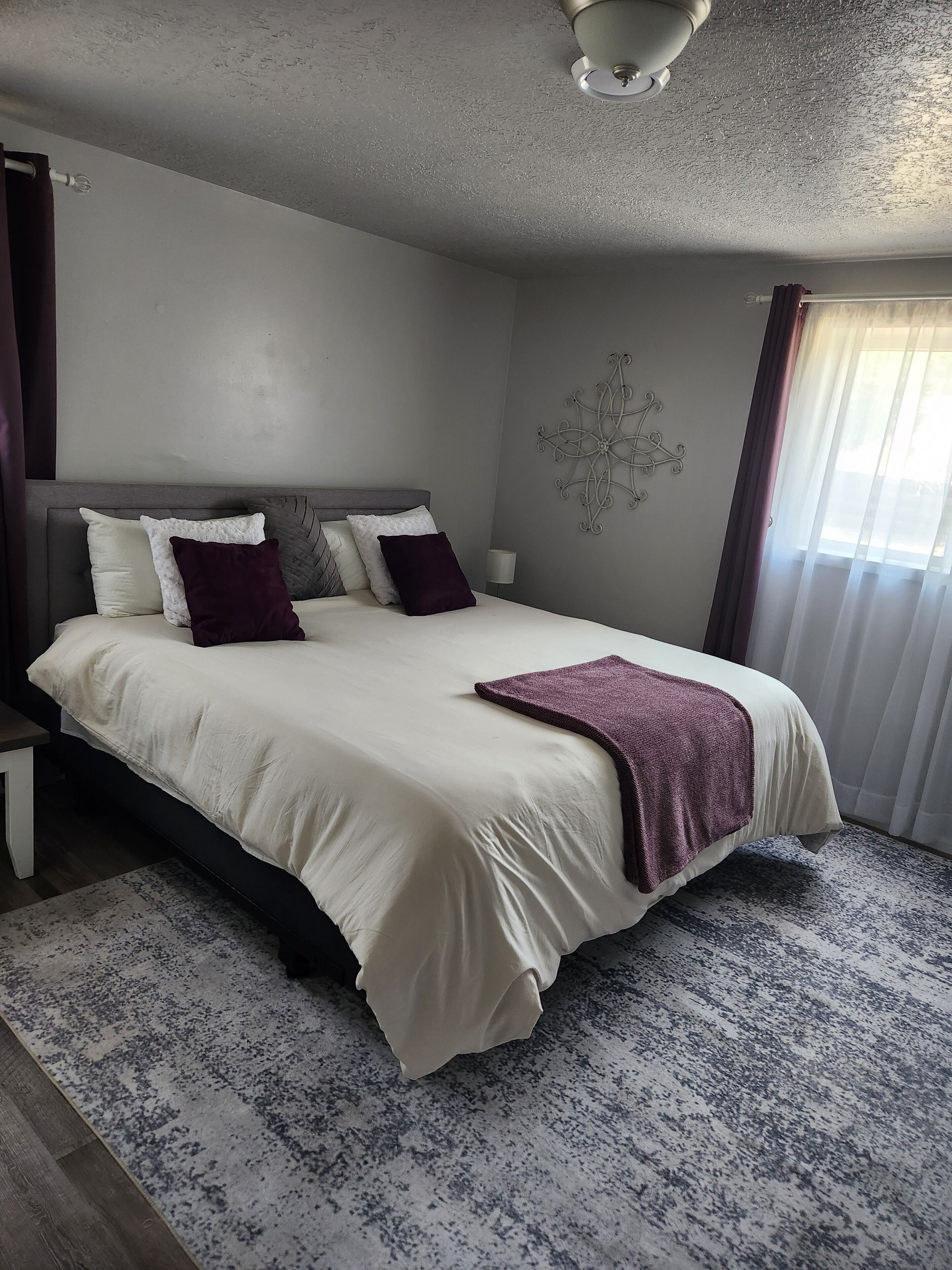 Une chambre à coucher comprenant un lit, une table de chevet, un luminaire fixé au mur et un élément décoratif mural.